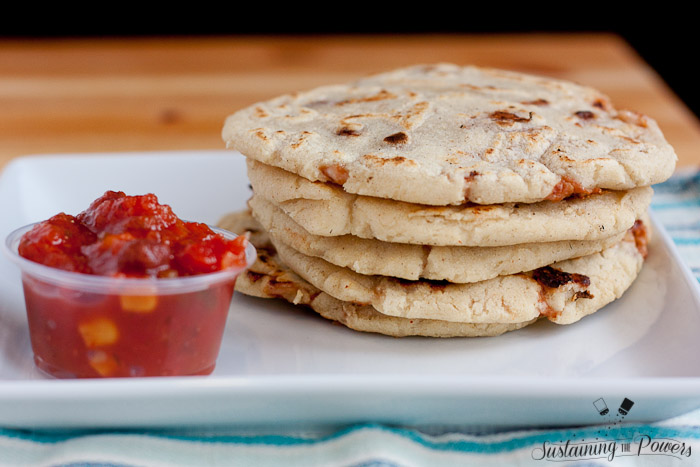 A large stack of bean and cheese stuffed corn pupusas with a cup of salsa.