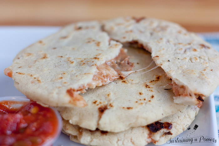 A pupusa pulled in half with strings of melted cheese.