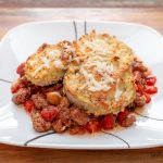 A plate of eggplant parmesan on top of a meat sauce