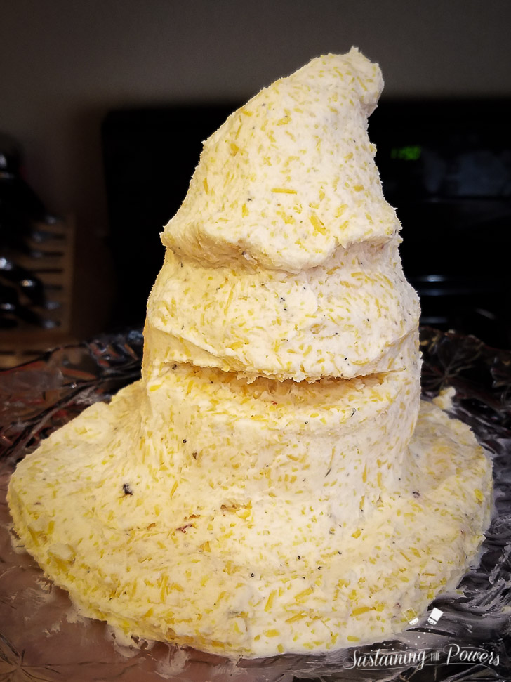 A cheese ball shaped like the sorting hat from Harry Potter, covered in poppy seeds and surrounded by crackers