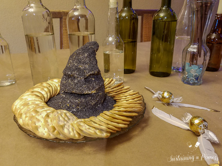 A cheese ball shaped like the sorting hat from Harry Potter, covered in poppy seeds and surrounded by crackers