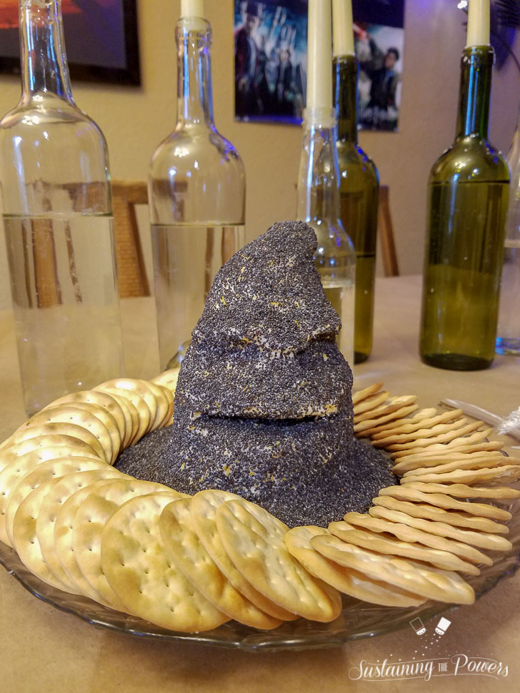 A cheese ball shaped like the sorting hat from Harry Potter, covered in poppy seeds and surrounded by crackers