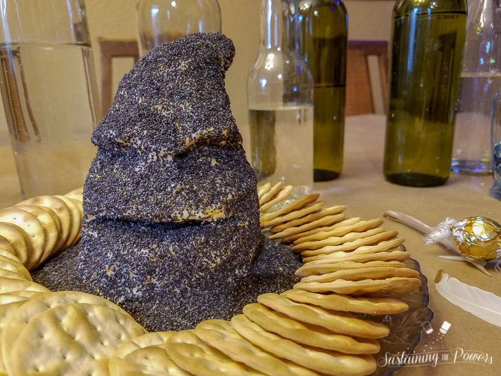 A cheese ball shaped like the sorting hat from Harry Potter, covered in poppy seeds and surrounded by crackers